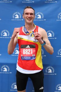 Picture of Jon Foxall sport massage therapist. He's smiling, holding a medal from the Boston Marathon.