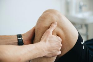 Image show a persons leg bend at the knee. A sport massage therapist has their hands between the bend, one from either side of the lower leg.